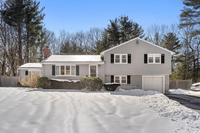 tri-level home featuring a garage, driveway, fence, and a chimney