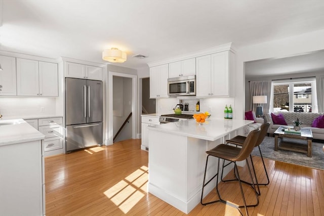 kitchen with white cabinets, open floor plan, light countertops, appliances with stainless steel finishes, and a kitchen bar