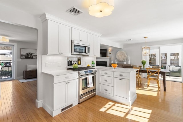 kitchen featuring a peninsula, white cabinetry, visible vents, and stainless steel appliances