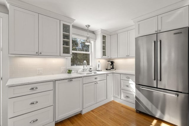 kitchen with decorative light fixtures, glass insert cabinets, white cabinets, a sink, and stainless steel refrigerator