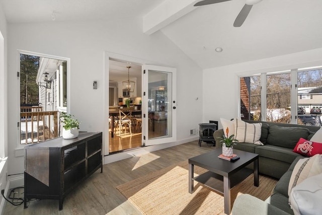 living area with lofted ceiling with beams, wood finished floors, a ceiling fan, baseboards, and a wood stove