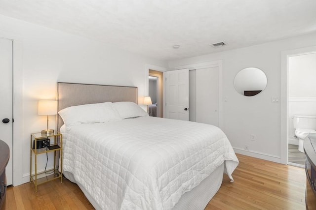 bedroom featuring ensuite bathroom, wood finished floors, visible vents, baseboards, and a closet