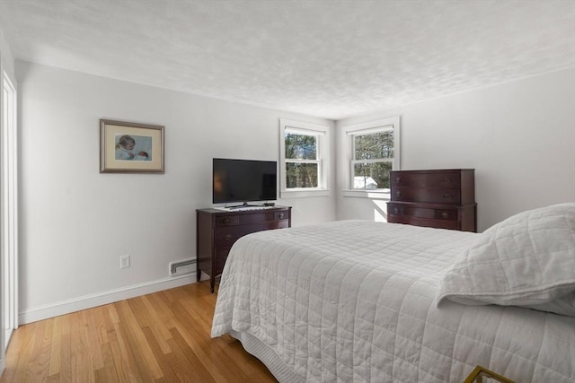 bedroom featuring light wood-style floors, a baseboard radiator, a textured ceiling, and baseboards