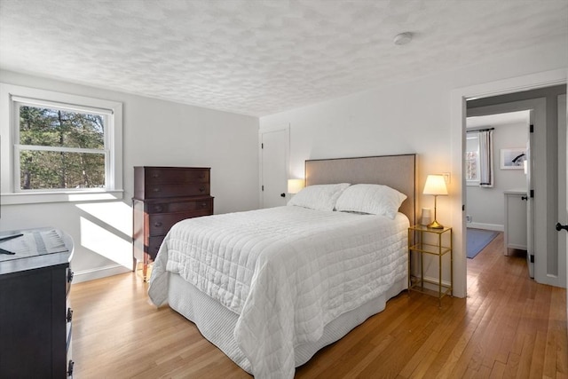 bedroom with a textured ceiling, baseboards, and light wood-style floors