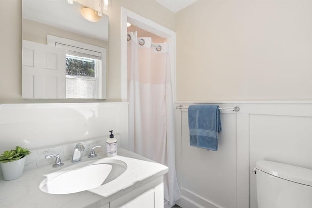 full bathroom featuring a shower with shower curtain, a wainscoted wall, vanity, and toilet