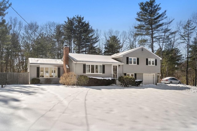 split level home with fence, a chimney, and an attached garage