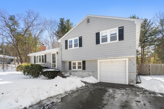 split level home with a garage, driveway, a chimney, and fence