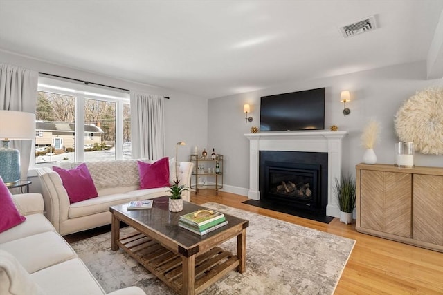 living area featuring baseboards, a fireplace with flush hearth, visible vents, and wood finished floors