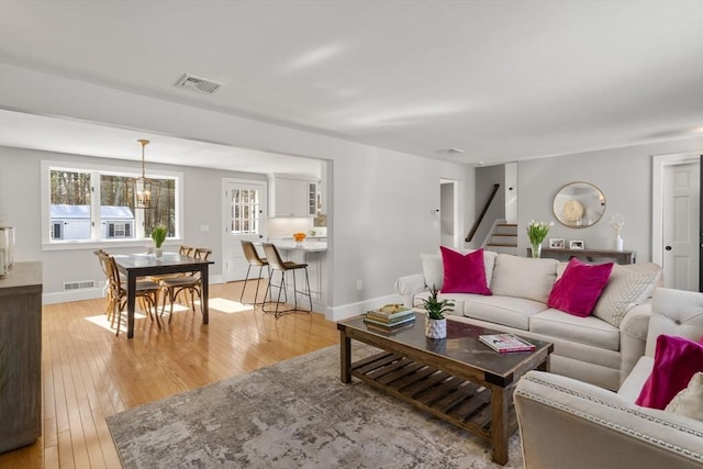 living area with stairs, baseboards, visible vents, and light wood-style floors