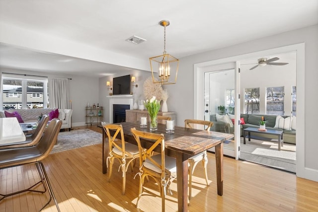 dining space with a fireplace, visible vents, light wood-style flooring, baseboards, and ceiling fan with notable chandelier