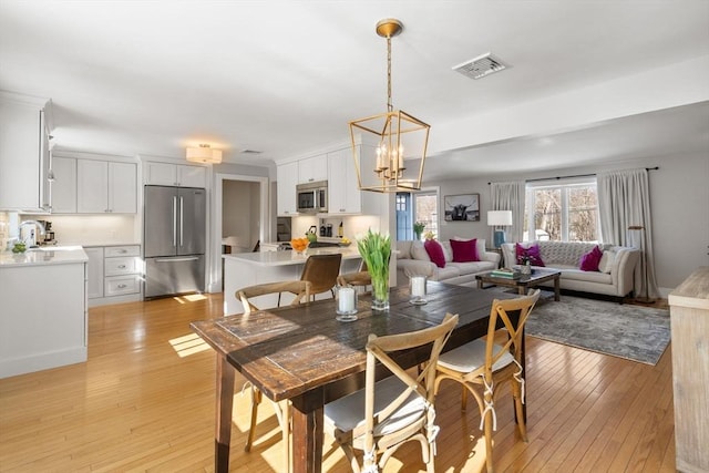 dining room with light wood-style floors, visible vents, and a notable chandelier