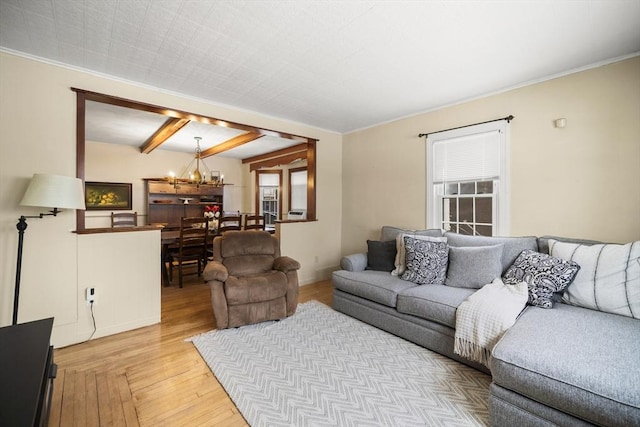 living room with beam ceiling, ornamental molding, an inviting chandelier, and light wood-type flooring