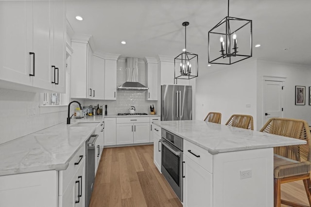 kitchen with a kitchen breakfast bar, stainless steel appliances, a kitchen island, and wall chimney range hood