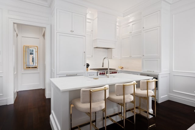 kitchen with dark wood-type flooring, white cabinets, an island with sink, and a breakfast bar