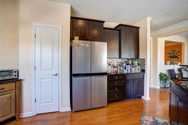 kitchen with dark brown cabinetry, baseboards, backsplash, freestanding refrigerator, and light wood finished floors