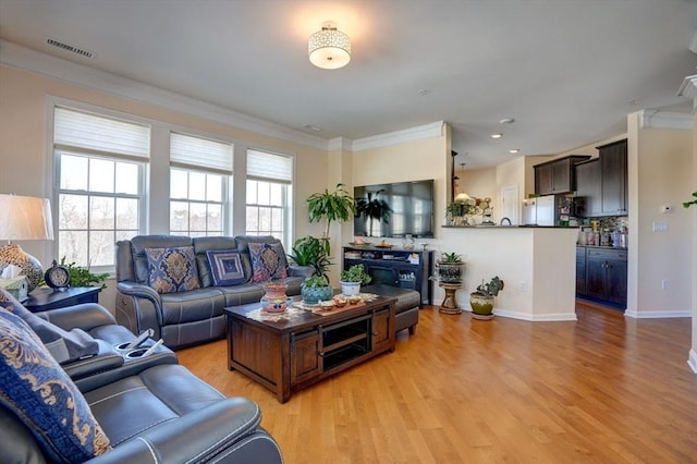 living room with ornamental molding, a wealth of natural light, visible vents, and light wood-style flooring