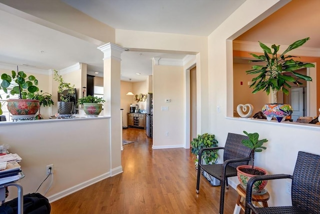 corridor featuring crown molding, baseboards, wood finished floors, and ornate columns