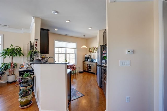 kitchen featuring visible vents, dark countertops, light wood-style flooring, freestanding refrigerator, and decorative light fixtures