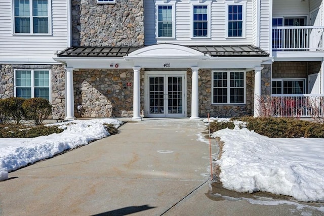 snow covered property entrance with a standing seam roof, stone siding, metal roof, and french doors