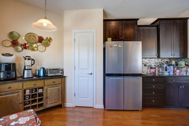 kitchen featuring a toaster, backsplash, freestanding refrigerator, dark brown cabinetry, and wood finished floors