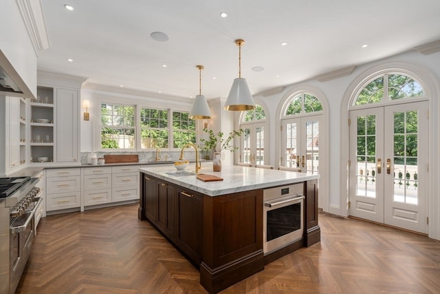 kitchen with oven, white cabinetry, a center island with sink, and light stone countertops