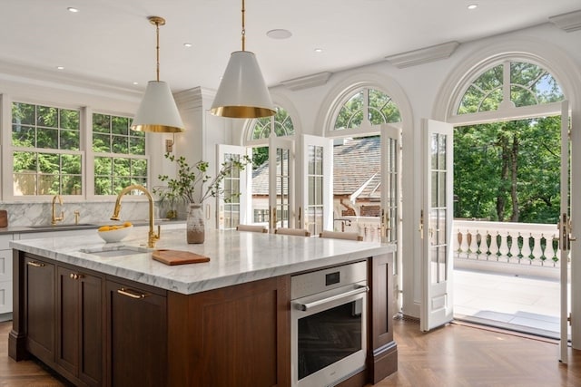 kitchen with light stone countertops, hanging light fixtures, oven, and sink