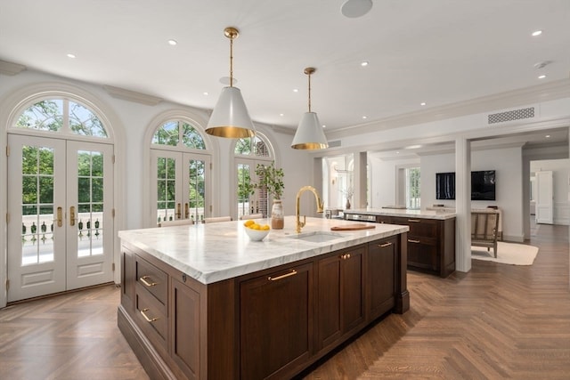 kitchen featuring pendant lighting, dark parquet flooring, sink, french doors, and a center island with sink