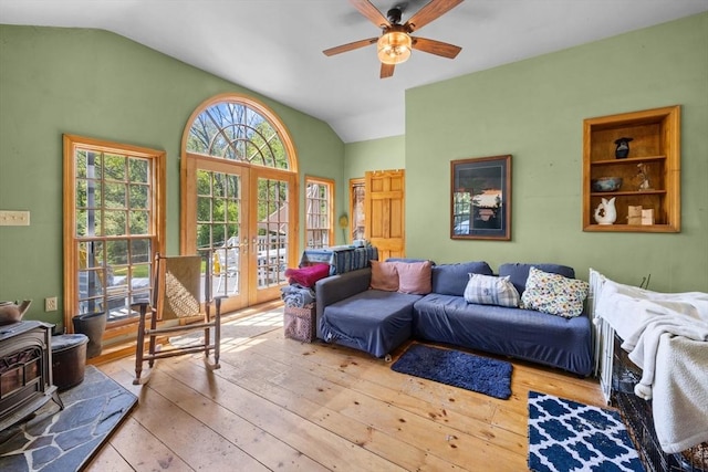 living room with french doors, vaulted ceiling, a ceiling fan, a wood stove, and hardwood / wood-style flooring