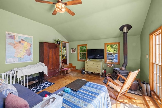 living room featuring a wood stove, vaulted ceiling, healthy amount of natural light, wood finished floors, and a ceiling fan