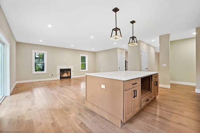 kitchen with pendant lighting, light wood-type flooring, a center island, light brown cabinets, and light stone countertops