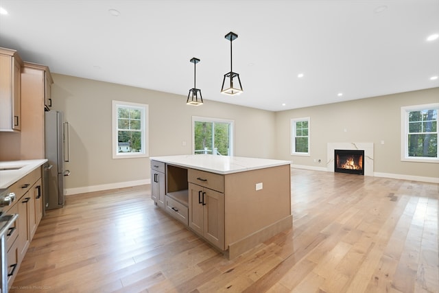 kitchen featuring pendant lighting, a premium fireplace, stainless steel refrigerator, a center island, and light wood-type flooring