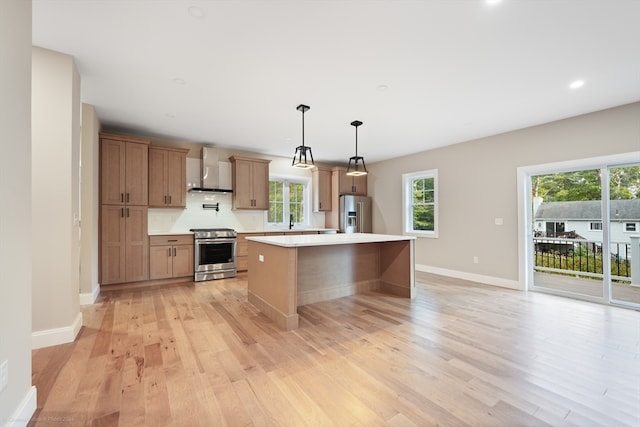 kitchen featuring light wood-type flooring, hanging light fixtures, a kitchen island, wall chimney range hood, and appliances with stainless steel finishes