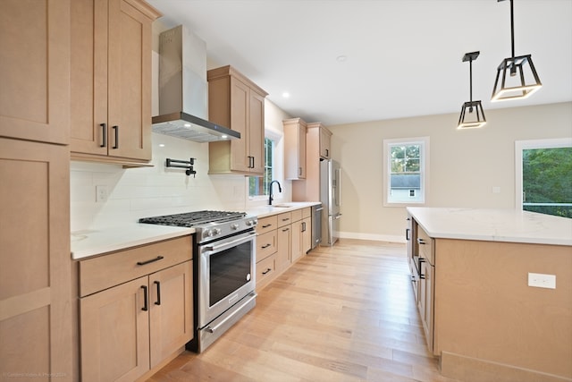 kitchen with appliances with stainless steel finishes, hanging light fixtures, wall chimney exhaust hood, light wood-type flooring, and sink