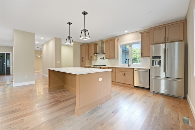 kitchen featuring decorative light fixtures, wall chimney range hood, stainless steel appliances, a center island, and light wood-type flooring