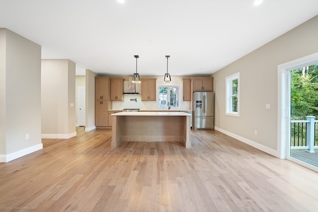 kitchen with light wood-type flooring, stainless steel fridge, a center island, and hanging light fixtures