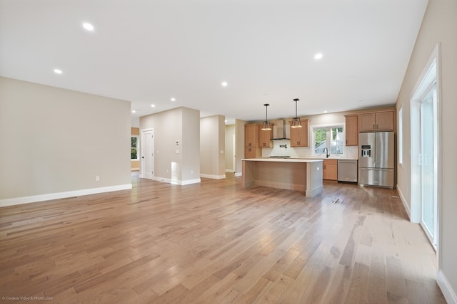 kitchen with decorative light fixtures, appliances with stainless steel finishes, wall chimney exhaust hood, and light hardwood / wood-style flooring