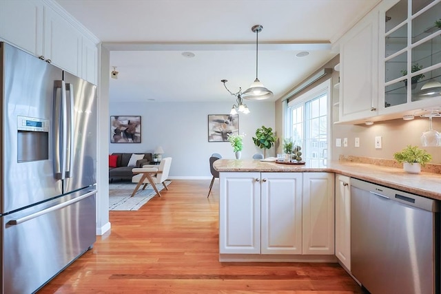 kitchen featuring white cabinets, hanging light fixtures, light wood-type flooring, and appliances with stainless steel finishes