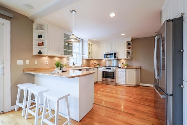 kitchen with kitchen peninsula, appliances with stainless steel finishes, light stone countertops, white cabinetry, and hanging light fixtures