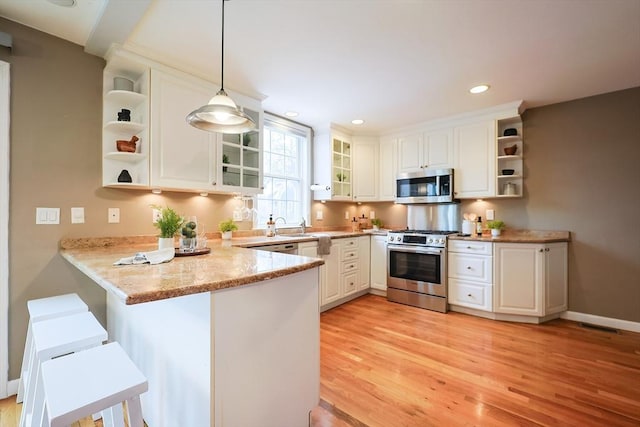 kitchen featuring kitchen peninsula, appliances with stainless steel finishes, light stone counters, white cabinets, and hanging light fixtures