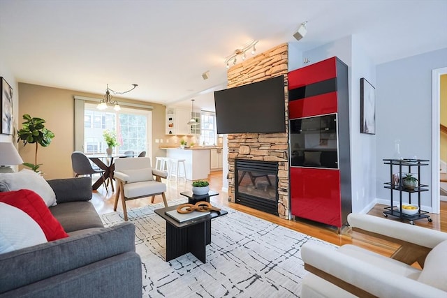 living room featuring a chandelier, light wood-type flooring, and a stone fireplace