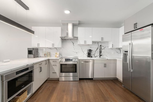 kitchen with a sink, wall chimney range hood, white cabinets, stainless steel appliances, and dark wood-style flooring