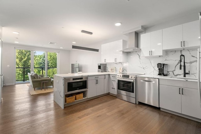 kitchen featuring backsplash, appliances with stainless steel finishes, a peninsula, wall chimney exhaust hood, and a sink