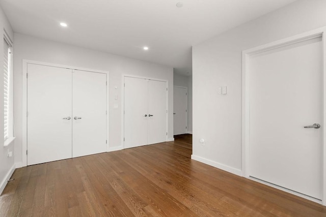 unfurnished bedroom featuring recessed lighting, baseboards, multiple closets, and wood finished floors