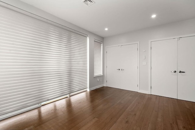 unfurnished bedroom with recessed lighting, wood finished floors, visible vents, and two closets