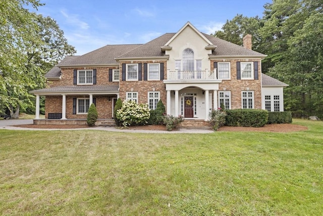 colonial house featuring a chimney, brick siding, a balcony, and a front lawn