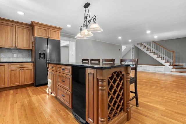 17 Topsfield Rd, Wenham, MA 01984 - kitchen featuring black refrigerator with ice dispenser, a breakfast bar area, dark countertops, brown cabinetry, and light wood-type flooring