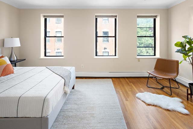 bedroom with crown molding, multiple windows, baseboard heating, and light hardwood / wood-style floors