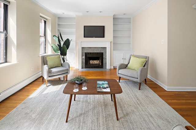 living room with built in shelves, ornamental molding, a tile fireplace, and hardwood / wood-style flooring