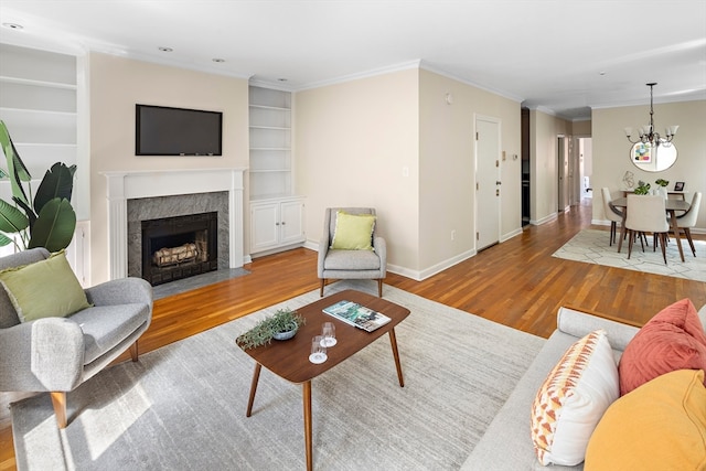 living room with built in shelves, ornamental molding, a notable chandelier, and light hardwood / wood-style flooring