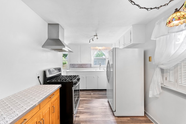 kitchen with light wood-type flooring, sink, wall chimney range hood, stainless steel gas range, and white fridge